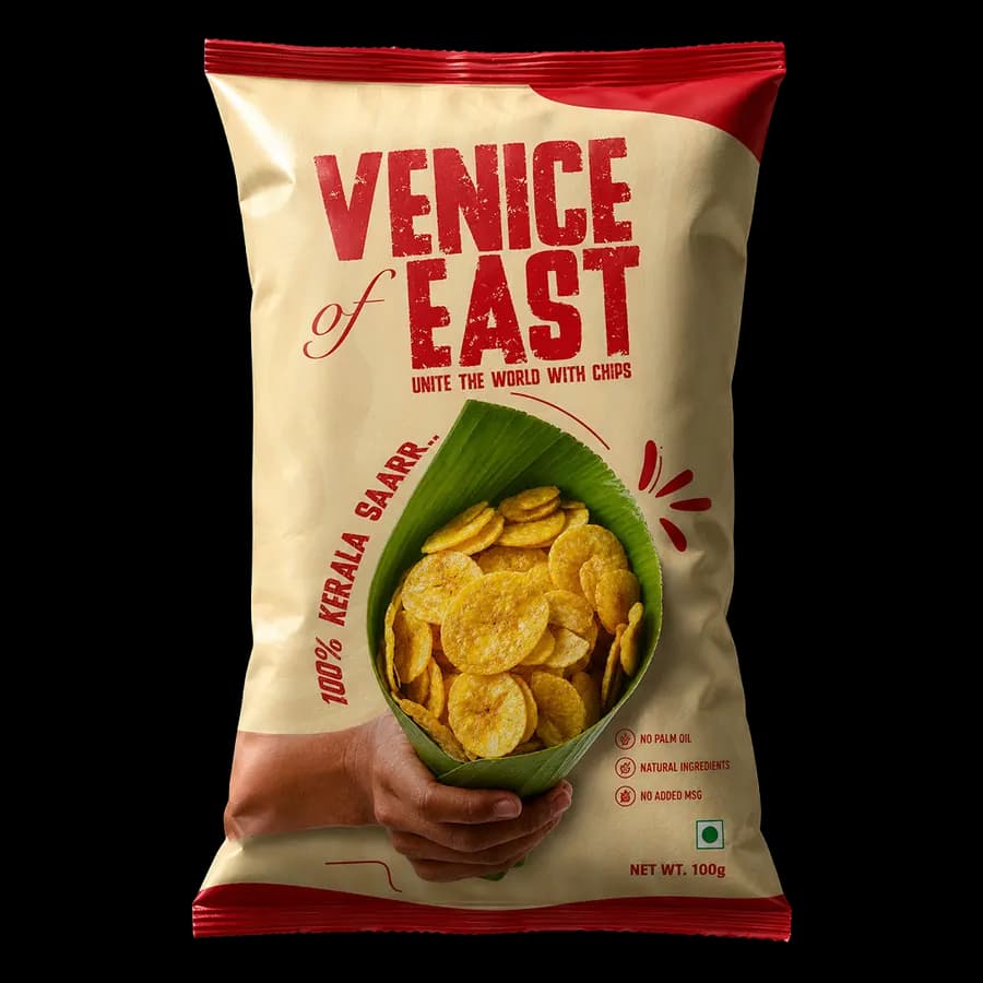 Cream and red Venice of East pack held in a hand, filled with banana chips in a green leaf, labelled 100% Kerala.